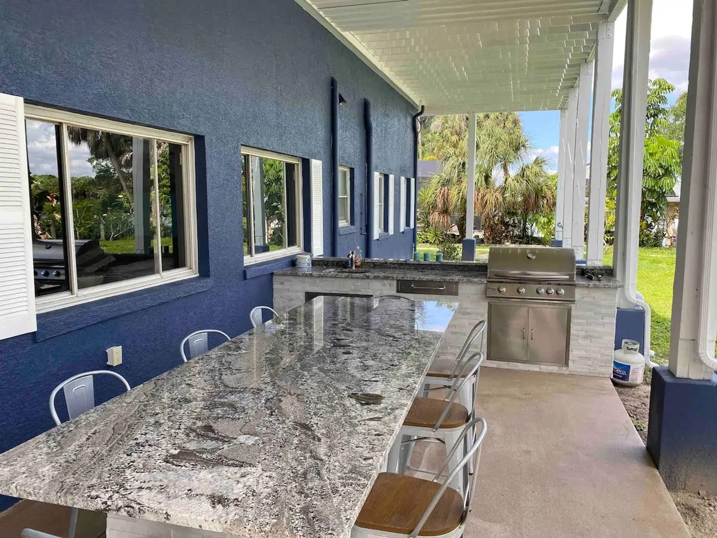 Granite breakfast bar with metal stools running along a covered lanai beside a built-in grill